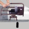 A person holds onto the Freedom Click Extendable Bed Rail with a communication pouch and built-in storage compartments, attached to a bed. A water bottle and small item rest in the compartments.