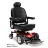 The Jazzy Elite ES is a red motorized wheelchair featuring black leather seating and joystick control, with large rear wheels and smaller front wheels. It is classified as an FDA Class II Medical Device.