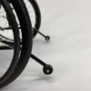 Close-up of the Feather Light 18 Wheelchairs black wheels on a smooth, light-colored surface, with a small stabilizer wheel visible in the background.