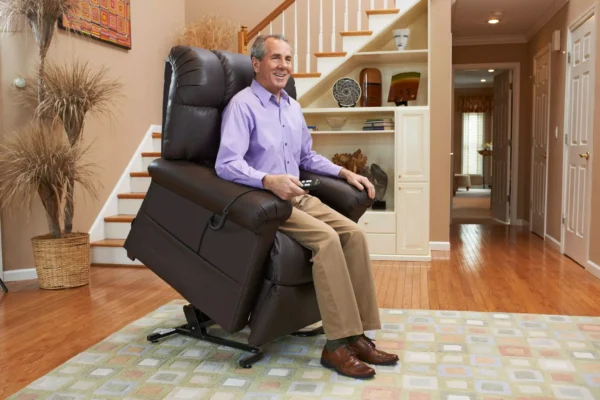 A person sits comfortably on a reclining chair in a living room, using a remote control. The room features wooden floors, a patterned rug, and a staircase in the background. Decorations include a basket and wall art.