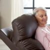 An older woman with short gray hair relaxes comfortably in a Golden Technologies®️ Cloud+ Power Lift Recliner PR 511. Shes wearing a pink sweater, smiling with her eyes closed as soft natural light filters through a window in the background.