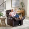An older woman with gray hair relaxes joyfully in a Golden Technologies®️ Cloud+ Power Lift Recliner PR 511. She wears a pink sweater and jeans in a modern room adorned with plants and a large painting.