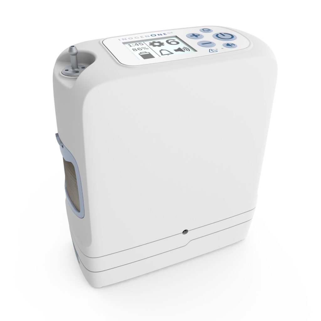 A white Inogen One G5 portable oxygen concentrator. The device features a digital display and several control buttons on the top. Its compact design includes a handle for easy carrying.